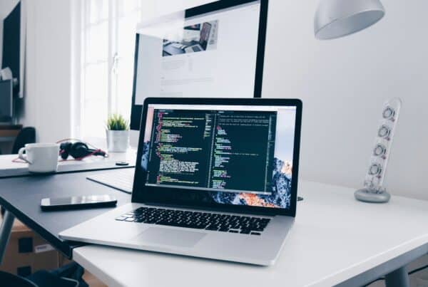 MacBook showing code on a desk in a bright office