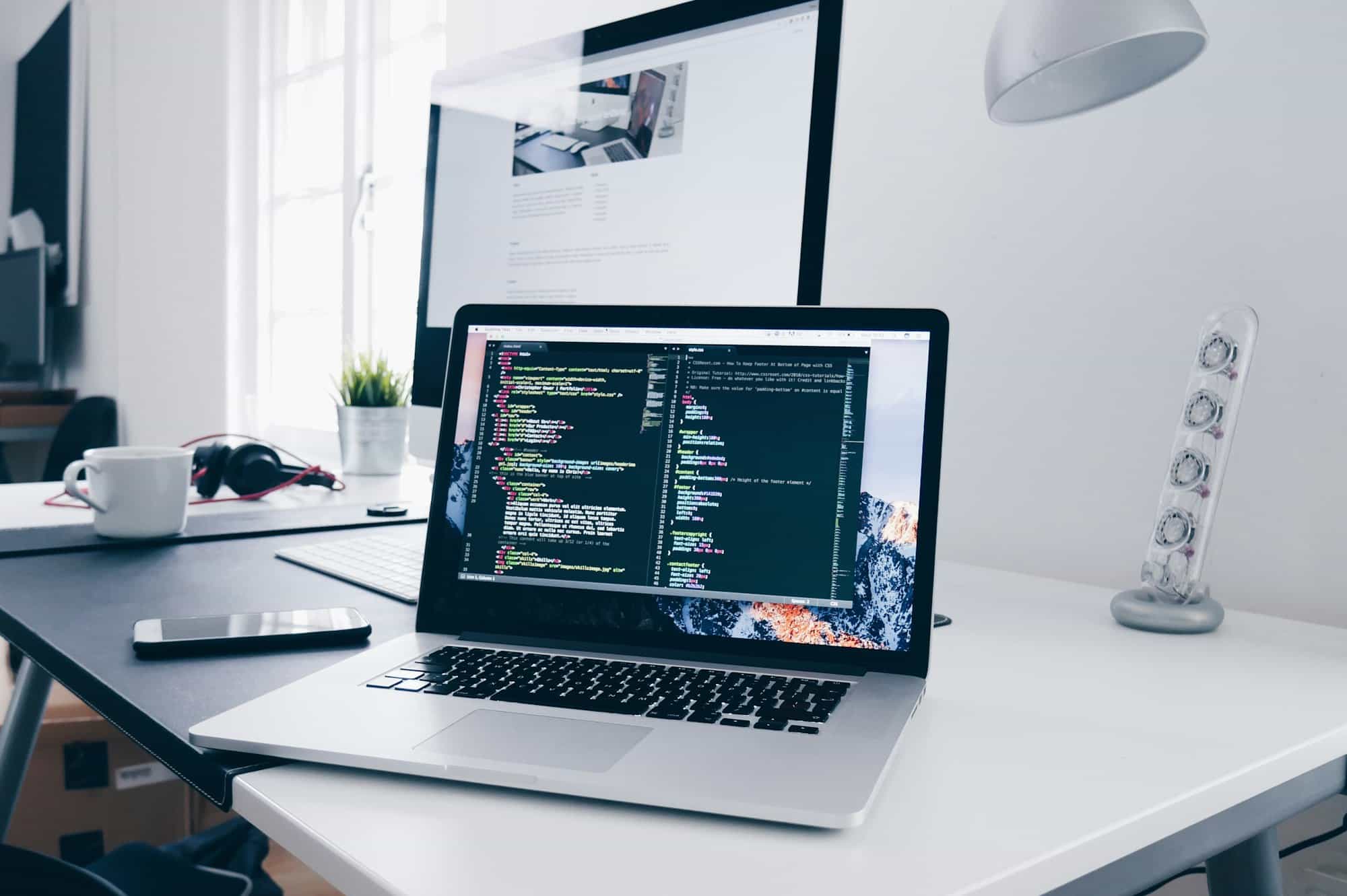 MacBook showing code on a desk in a bright office